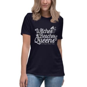 A woman models a relaxed fit, dark navy t-shirt featuring white text that reads "Witches Beaches Queens" with a mermaid graphic, and "New Smyrna Beach, Florida" below.
