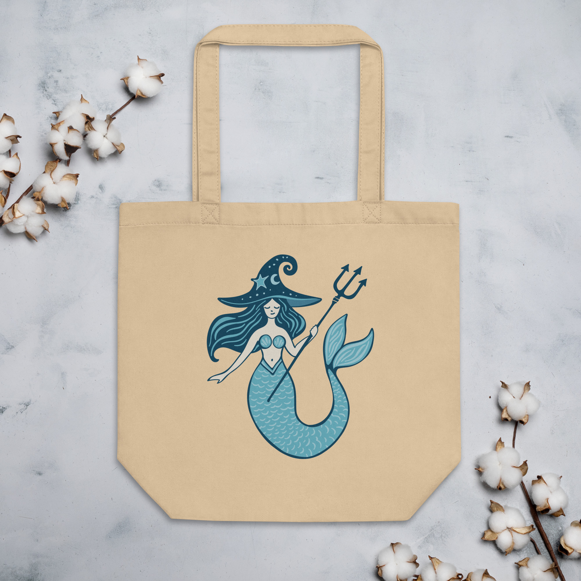 A witchy mermaid with a teal witch hat and trident adorns a beige tote bag, a magical accessory perfect for any witchy errand.